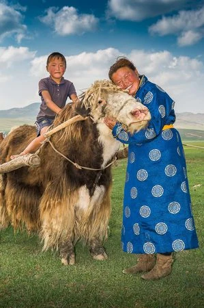 Mongolská žena s dítětem objímá koně na zelené stepi.