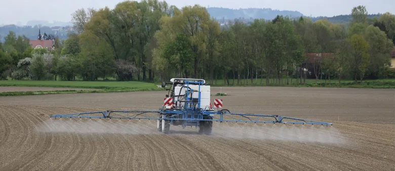 Modrý traktor postřikuje pole pesticidy v krajině.