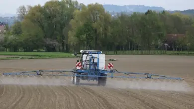 Modrý traktor postřikující pole pesticidy v krajině.