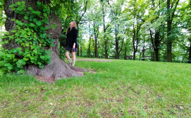 Žena stojí u tlustého kmene stromu v parc.