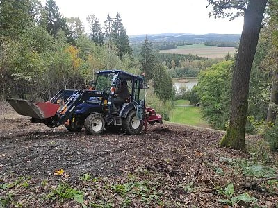 Traktor odstraňuje náletové dřeviny na pozemku u jezera.