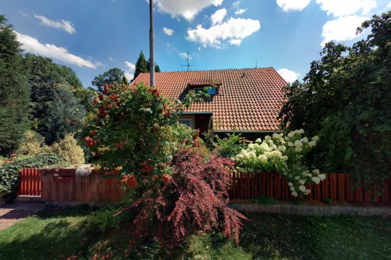Dům s zahradou plnou zeleně a kvetoucích rostlin.