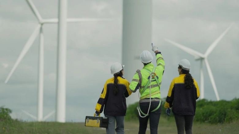 Tři pracovníci u větrných turbín ukazují na konstrukci.