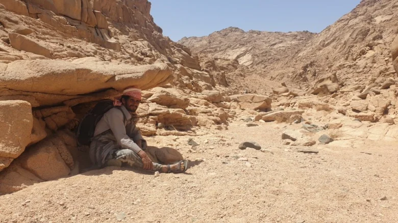 Beduíni muž sedí pod skalním úkrytem v poušti Egypta.