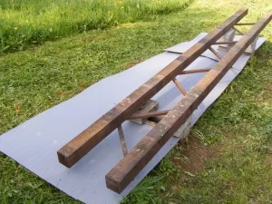 Dřevěný nástroj pro včelaře leží na šedé podložce ve trávě.